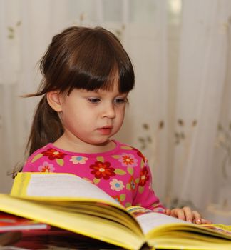 The child reading the book. The three-year girl in house conditions