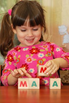 The girl and toy cubes. The child collecting a word mama from cubes.