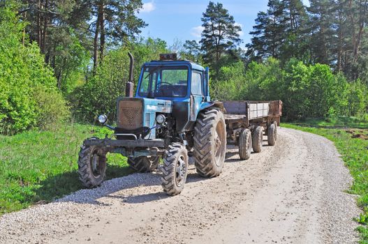 Tractor with trailer, country road in the forest, spring sunny day