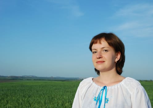 The Russian woman in national clothes. On a background of the sky and a field