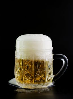 Glass of beer on a black background with the foam poured around