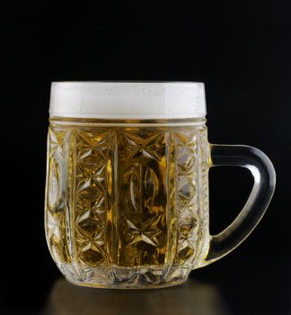 crystal cup of beer on a black background with the foam poured around