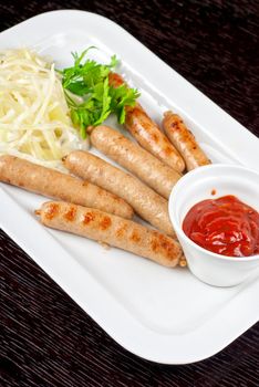 Grilled sausages with cabbage, greens and tomato sauce on white plate