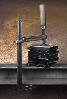 pressing  a stack of hard drives with a clamp in rusty background