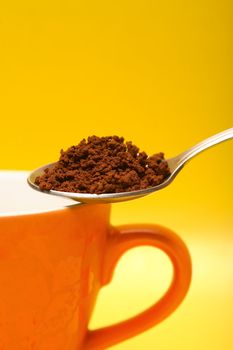 Closeup of spoon with instant coffee and cup on yellow background