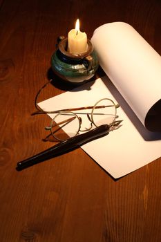 Scroll and old spectacles near lighting candle on wooden surface