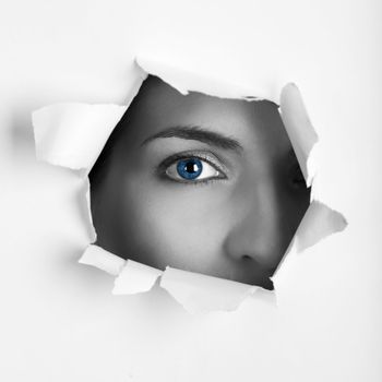 Beautiful female blue eye looking through a hole on a sheet of paper