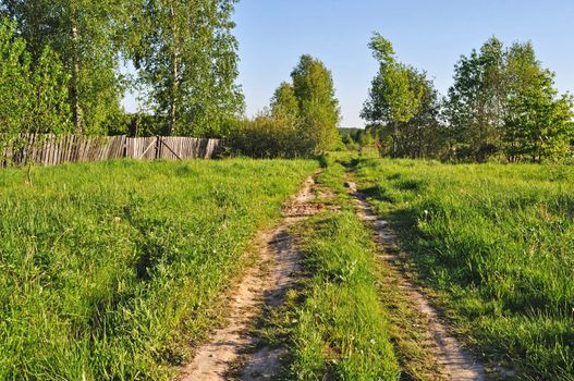 Country dirt road along the wooden fence at village outskirts on evening