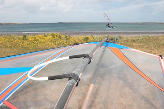 surfboard lying on the beach as a surfer windsurfs in the maharees in county kerry ireland during a storm