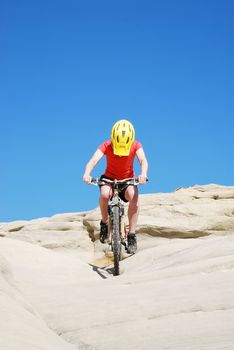 Mountain biker in red and orange against boulders and blue sky.