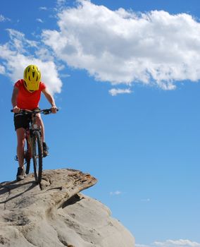 Mountain biker in red and orange against boulders and blue sky.