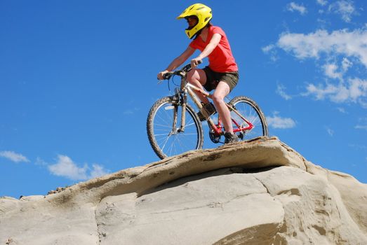 Mountain biker in red and orange against boulders and blue sky.