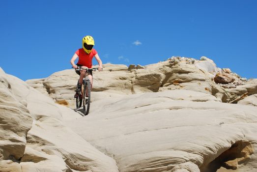 Mountain biker in red and orange against boulders and blue sky.