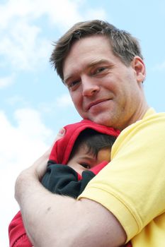 Baby cuddled safely in dad's arms. Father is Scandinavian, baby is multiracial