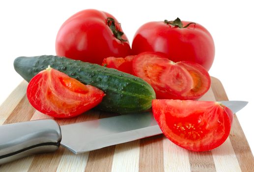 Vegetables (tomatos and cucumber) with knife on bamboo cutting board.