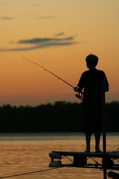 Silhouette of boy fishing off pier at sunset