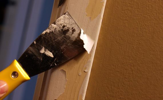 A close-up of a person stripping paint using a putty knife.
