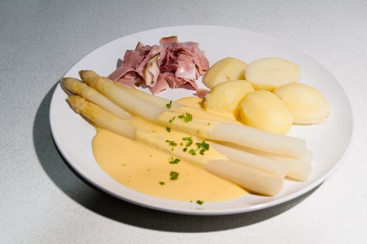 Meal with white asparagus and potatoes in sauce hollandaise.