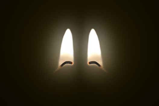 Close up on two ignited candle wicks against a black background.