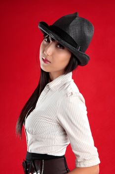 A beautiful mixed race asian / caucasian woman wearing a black hat,  striped shirt and black skirt against a striking red background.