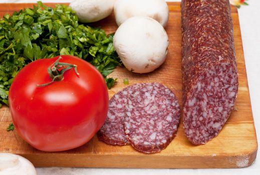 Some ingredients for pizza: parsley, sausage, tomatoes.