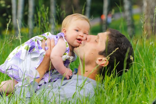 Happy father with his daughter resting in the grass on a meadow