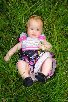 A beautiful little baby girl lying in the grass