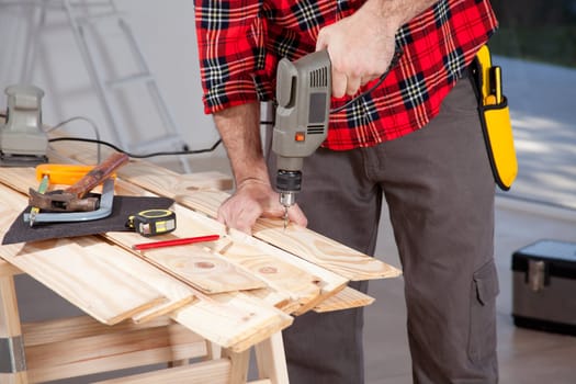 A male using an electric hand drill on a plank