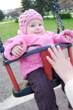 Baby girl in pink on swing in park