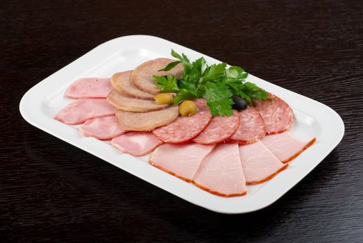 Meat assortment of beef tongue, sausage, meat and ham with greens
