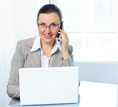 Attractive smiling young business woman with glasses using laptop at work desk