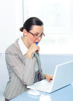 Attractive smiling young business woman with glasses using laptop at work desk