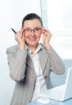 Attractive smiling young business woman with glasses using laptop at work desk