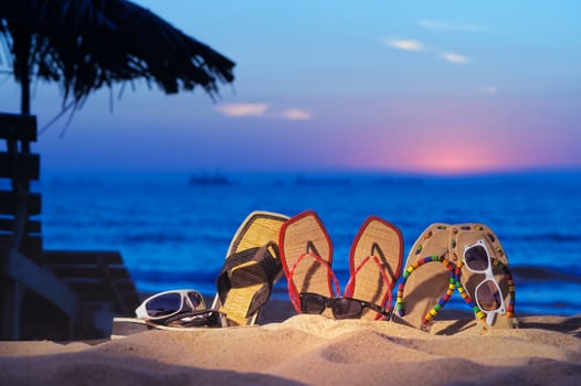 Three pair of beach sandals and glasses on the beach on evening