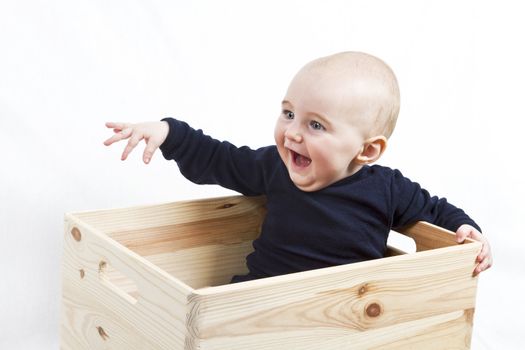 young child sitting in wooden box pointing to the left