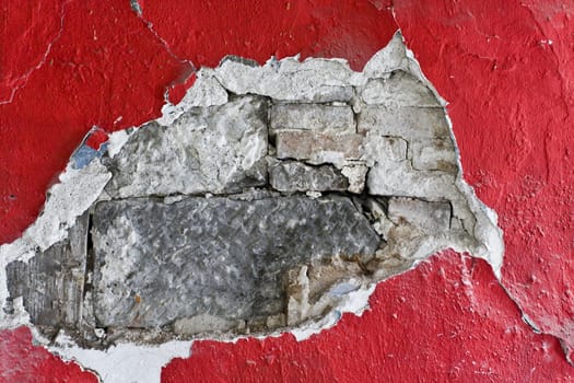 Old red wall with whole in red render with sandstone looking through