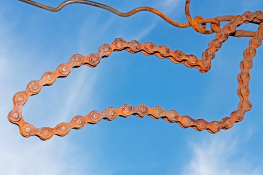 Old rusty steel chain hanging on the wire against blue sky