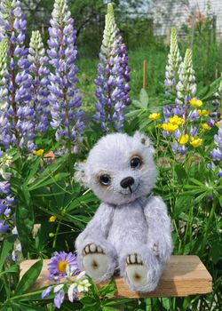 Handmade, the sewed toy: teddy bear Chupa on a little board among flowers lupine and buttercups