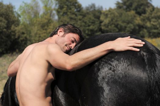 naked young man and black stallion in the nature, focus on the head