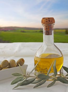 Oil, olives and olive branch over a white cloth, with beautiful sky on the background. 