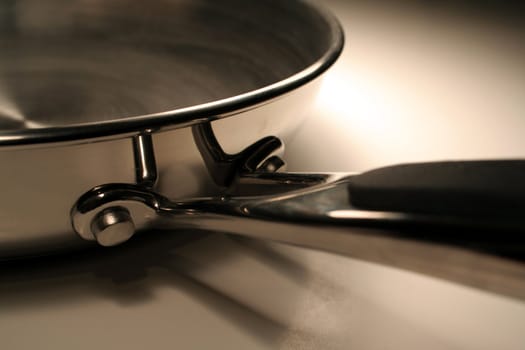 A close up of the handle of a stainless steel frying pan.
