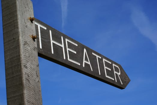 Wooden theater sign in shape of an arrow against a blue sky.           