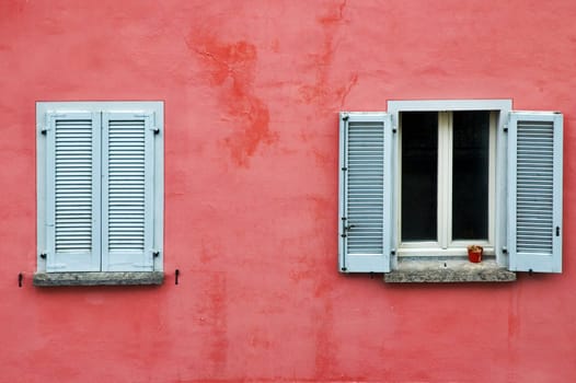 Two windows on a pink wall, one with white shutters closed