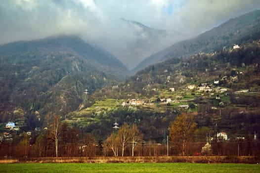 Spring mountains with dramatic clouds and green field in the foreground