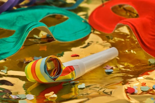 Close up of a party blower and masks on golden paper with confetti and selective focus