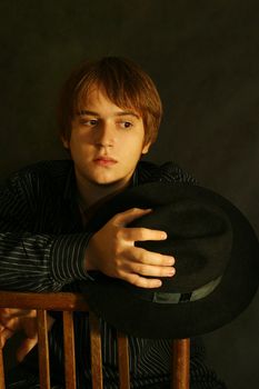 Portrait of the young man on a black background. In a hand a hat