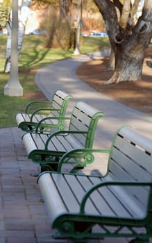 Vertical image of three unoccupied city park benches near a curving walking path.  Shallow depth of field.