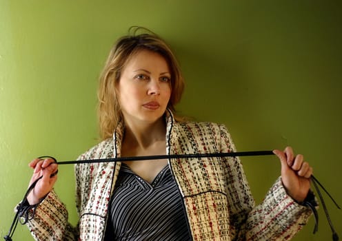 The image of the girl in a coat on a green background in hands a belt