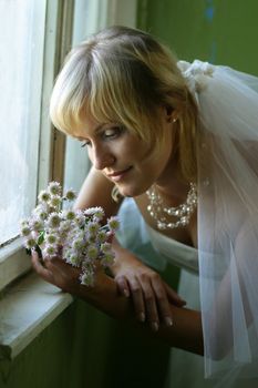 The beautiful girl in a wedding dress at a window with chrysanthemums