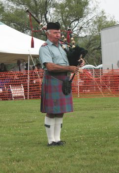 A piper playing with his band in a circle, competing against other pipe bands for honours. This piper is wearing the Ancient Lindsay tartan.
